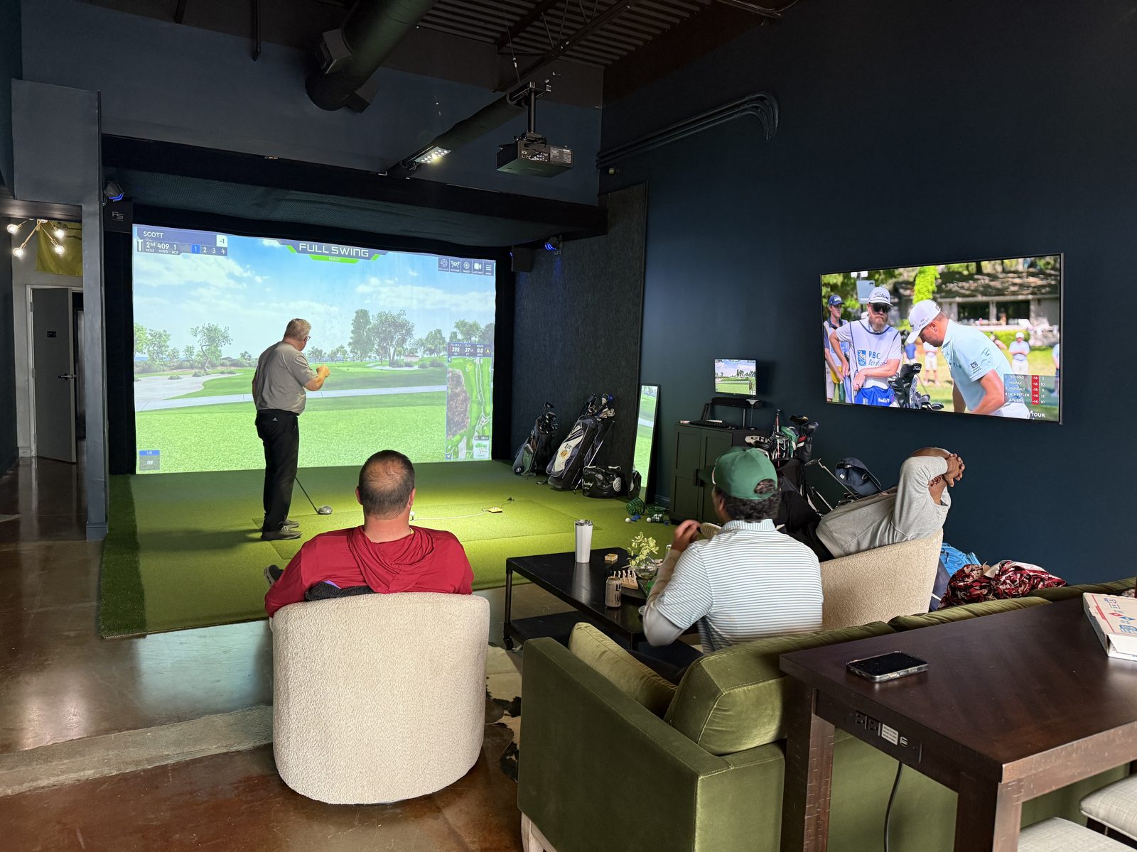 Golfer teeing off on the simulator while friends relax in swivel chairs
