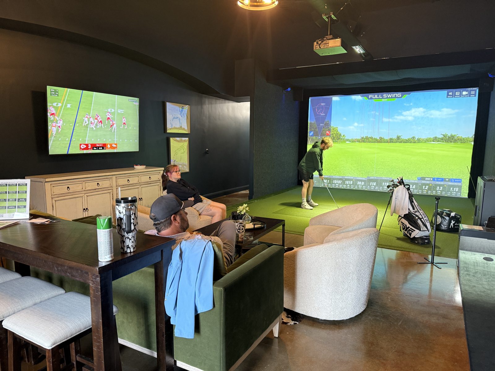Golfer hitting on the simulator with football on the lounge TV